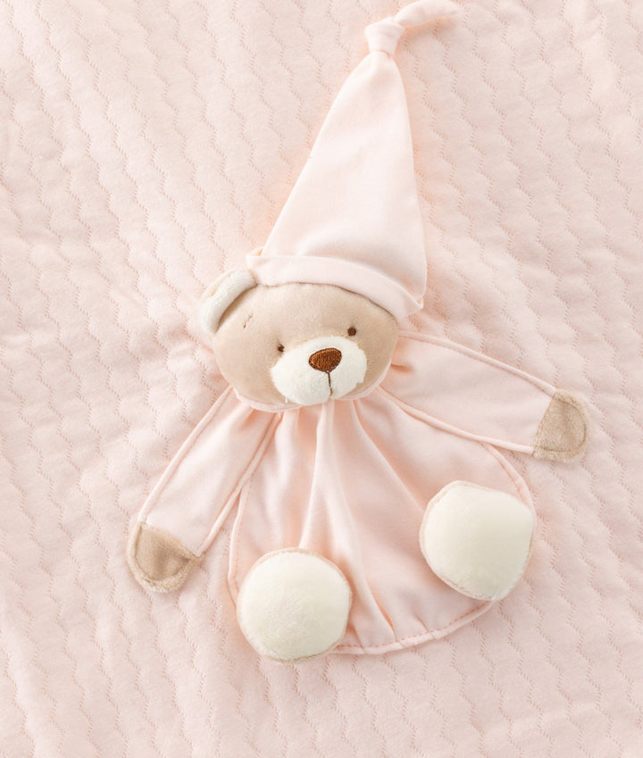 Pink baby blanket with plush bear wearing sleep cap on textured cotton