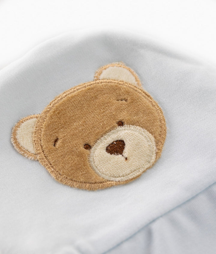 close up of embroidered brown teddy bear face patch detail on soft light blue baby hat fabric