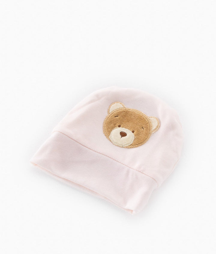 Close-up of light pink cotton beanie showing textured weave and brown bear applique