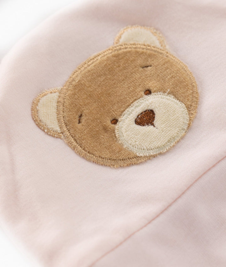 Macro view of embroidered brown teddy bear face patch on soft light pink cotton beanie