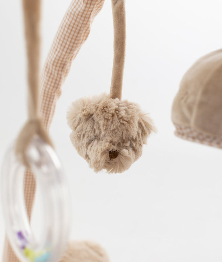 Close up of fluffy beige plush ball toy hanging next to clear plastic rattle ring on gym bar