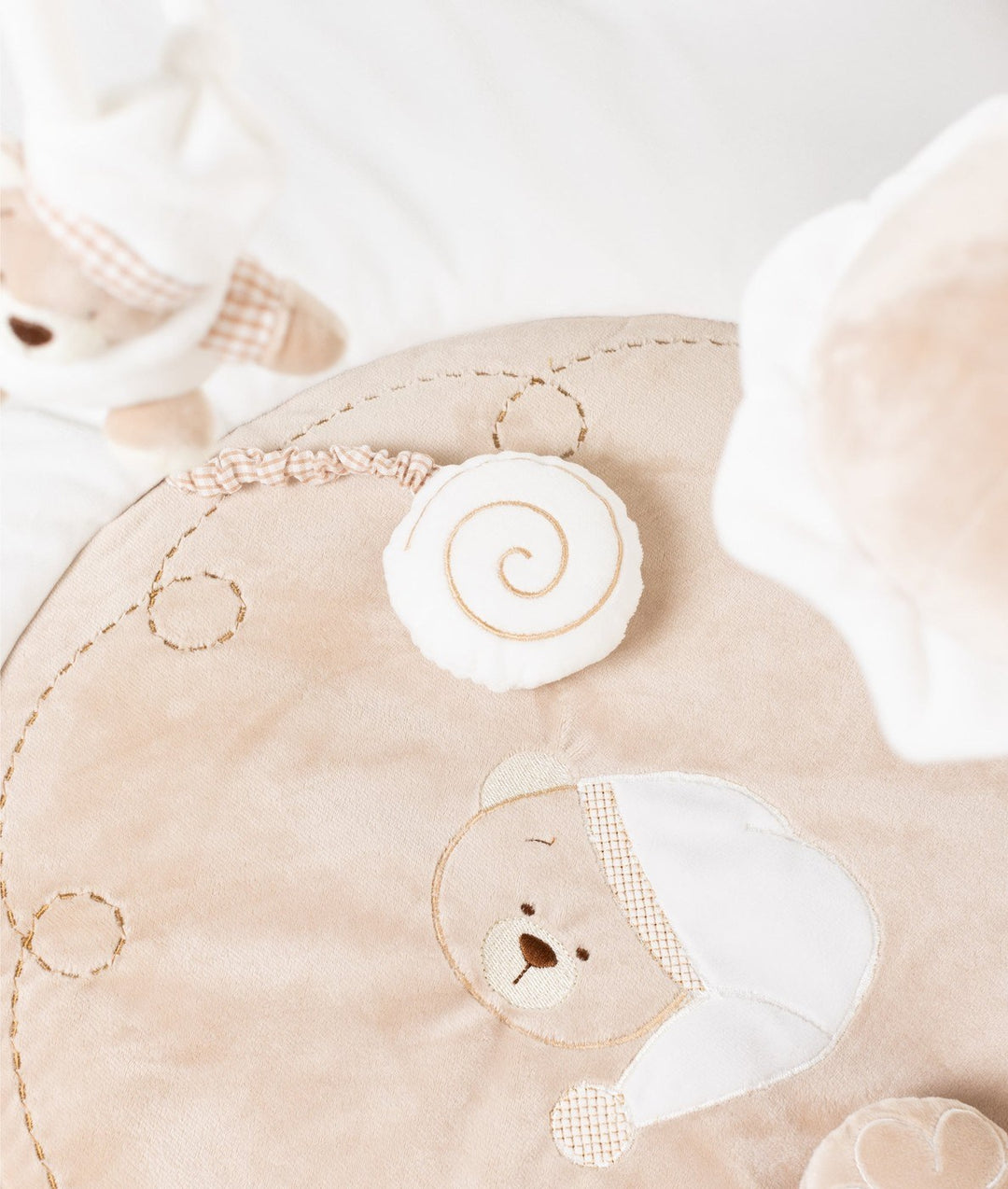 Macro detail of embroidered sleeping bear face and snail toy on beige playmat panel