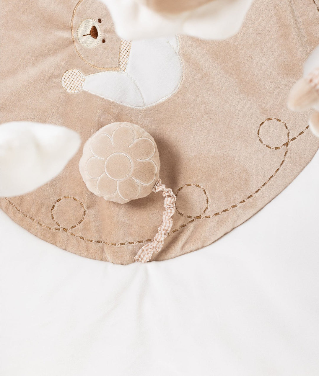 Detail of embroidered bear face and flower rattle on textured beige playmat fabric