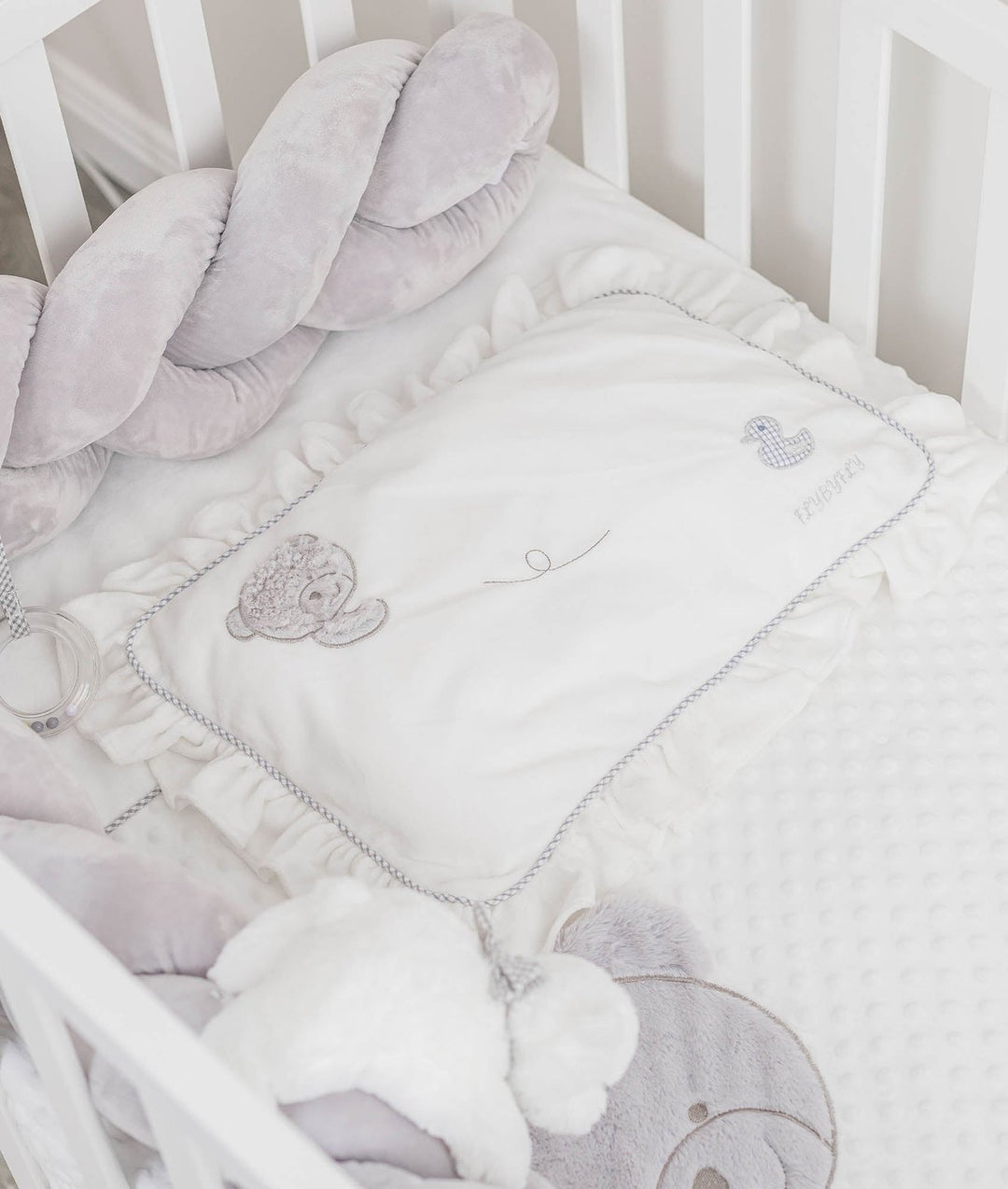 ruffled pillow with grey trim and embroidered details next to grey bumper