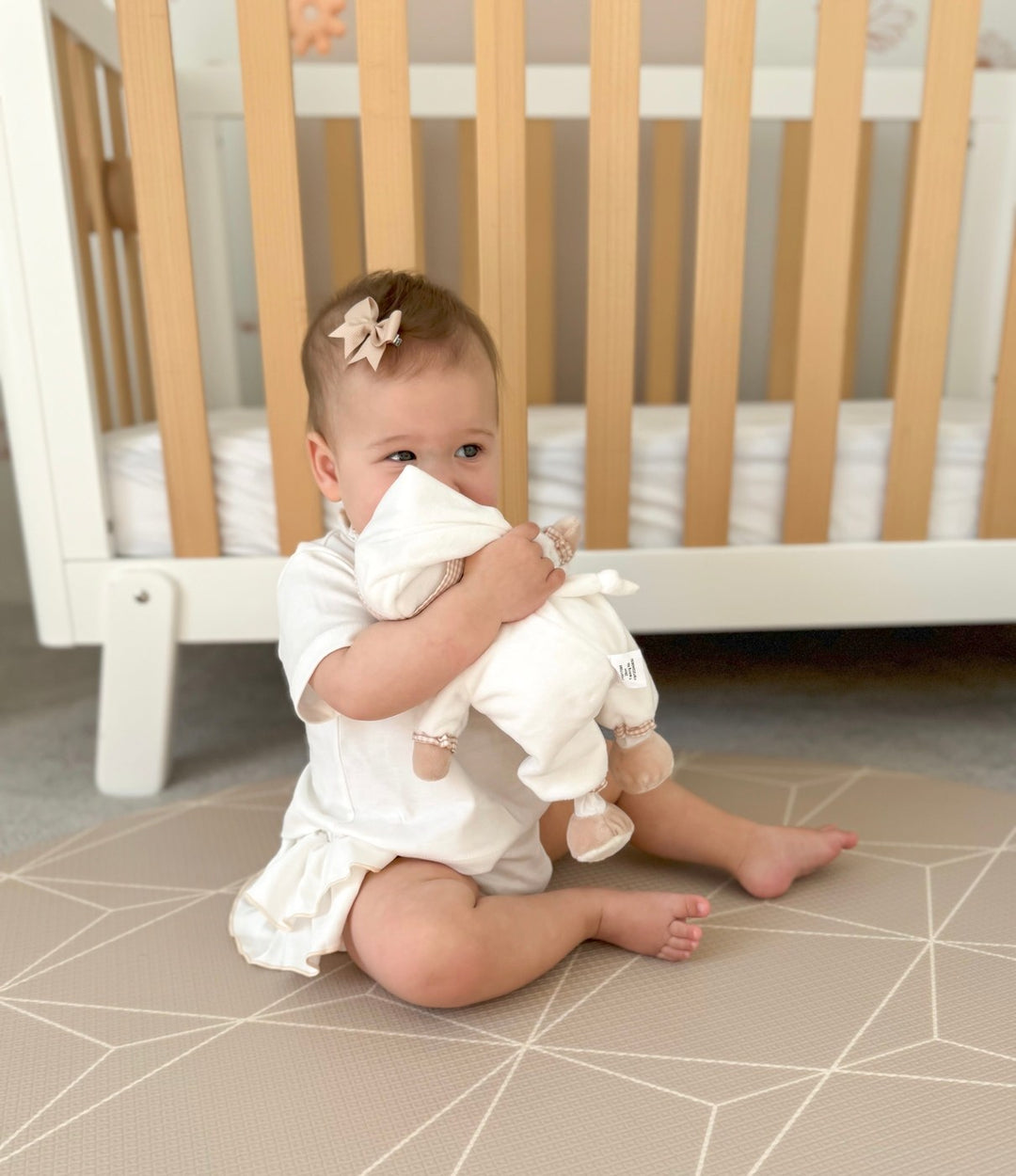 Baby holding Cuddle Bear plush toy close to face wearing matching bow hair clip