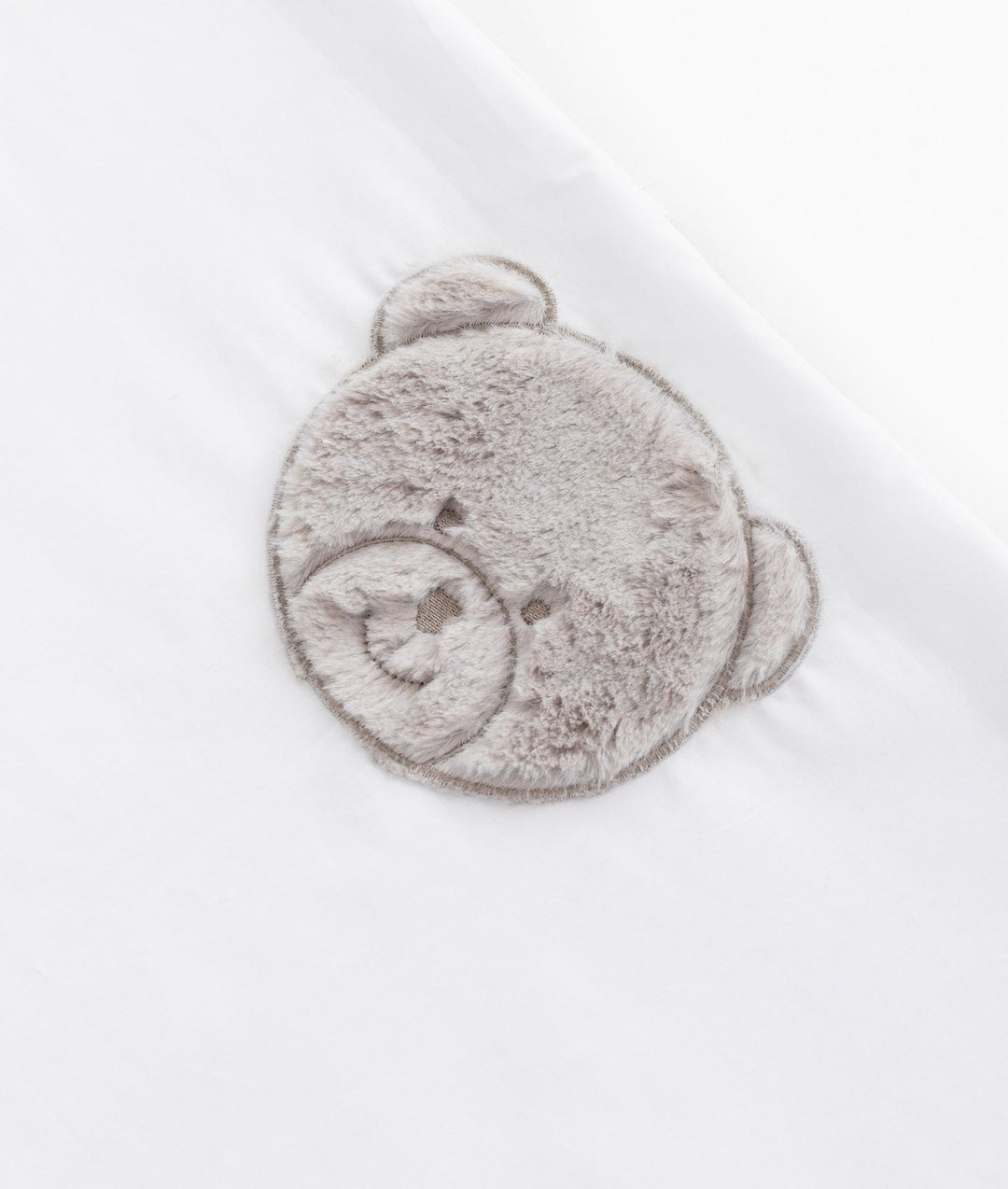 Macro texture of grey plush teddy bear embroidery on white cotton flat sheet