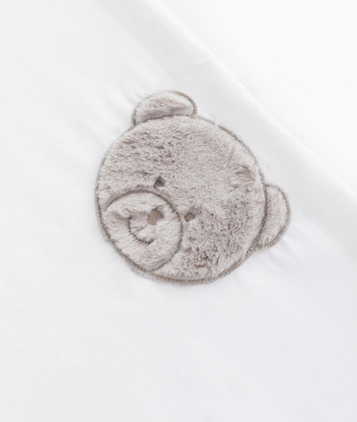 Macro texture of grey plush teddy bear embroidery on white cotton flat sheet