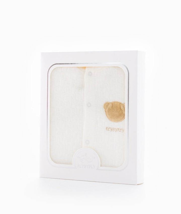 Cream hooded baby jumpsuit in white retail packaging with clear window revealing tan bear patch and FLYBYFLY logo seal