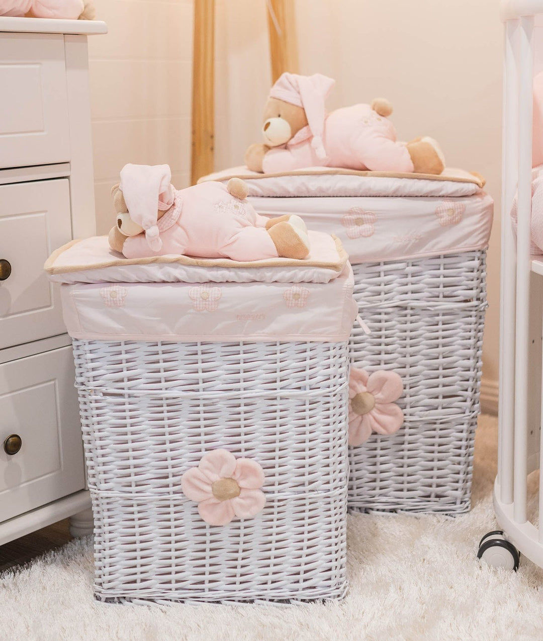White oval wooden cot bed with braided pink bumper pads and hanging mobile