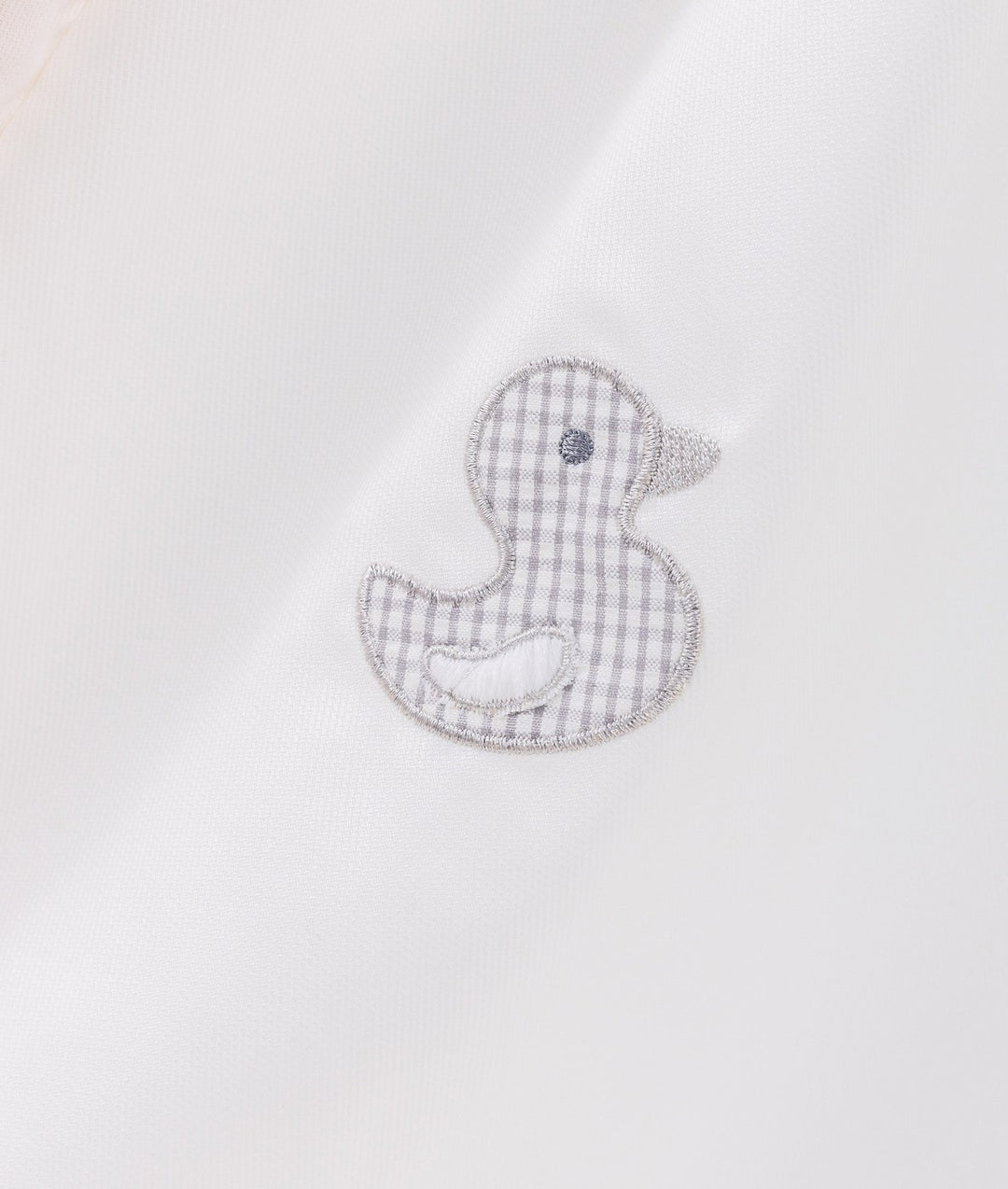 Macro shot of grey gingham rubber duck patch with silver thread on white canvas tent