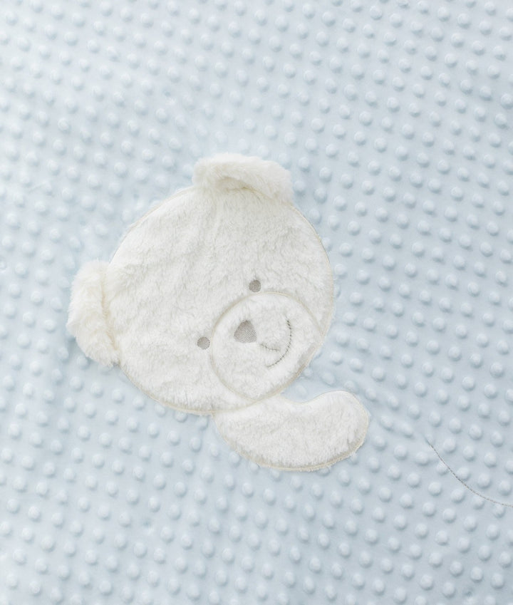 Macro view of white plush teddy bear face patch on light blue dotted minky fabric